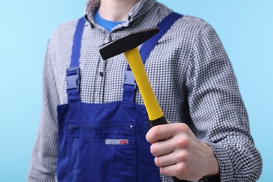 Professional repairman holding hammer on light blue background, closeup