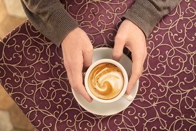 Photo of Young woman with cup of delicious coffee at table, top view