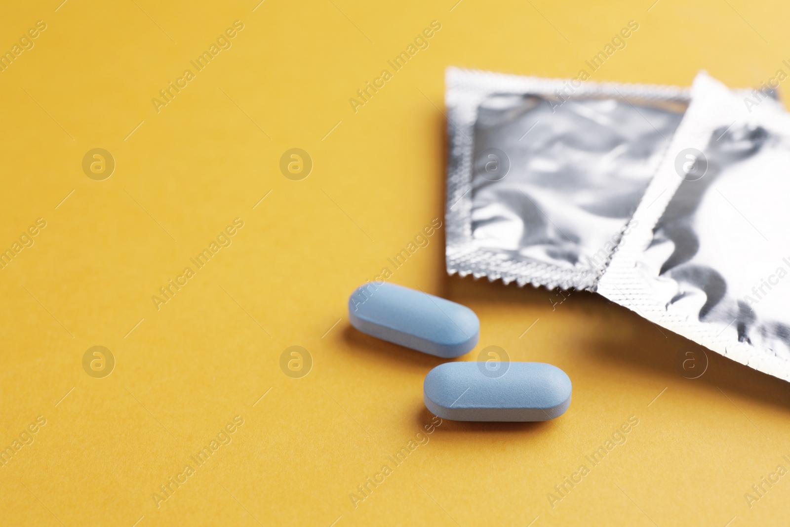 Photo of Pills and condoms on orange background, space for text. Potency problem