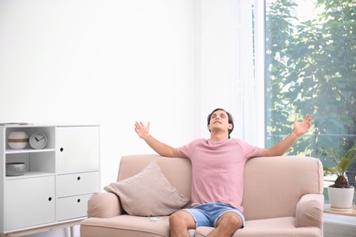 Young man relaxing under air conditioner at home