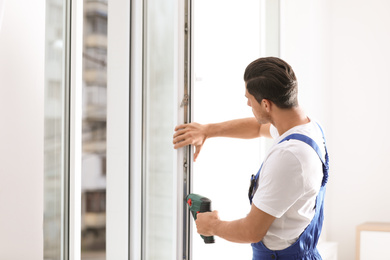 Photo of Construction worker repairing plastic window with screwdriver indoors