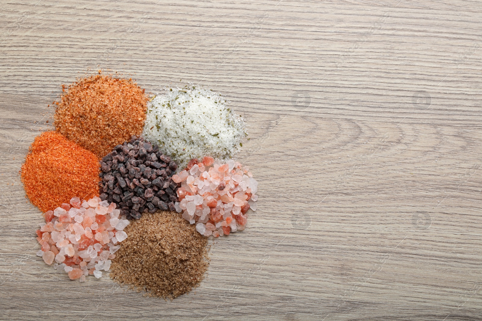 Photo of Different kinds of salt on wooden table, top view. Space for text