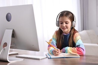 E-learning. Cute girl taking notes during online lesson at table indoors