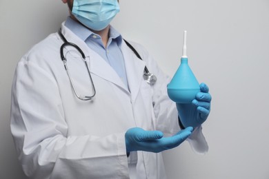 Photo of Doctor holding rubber enema on grey background, closeup