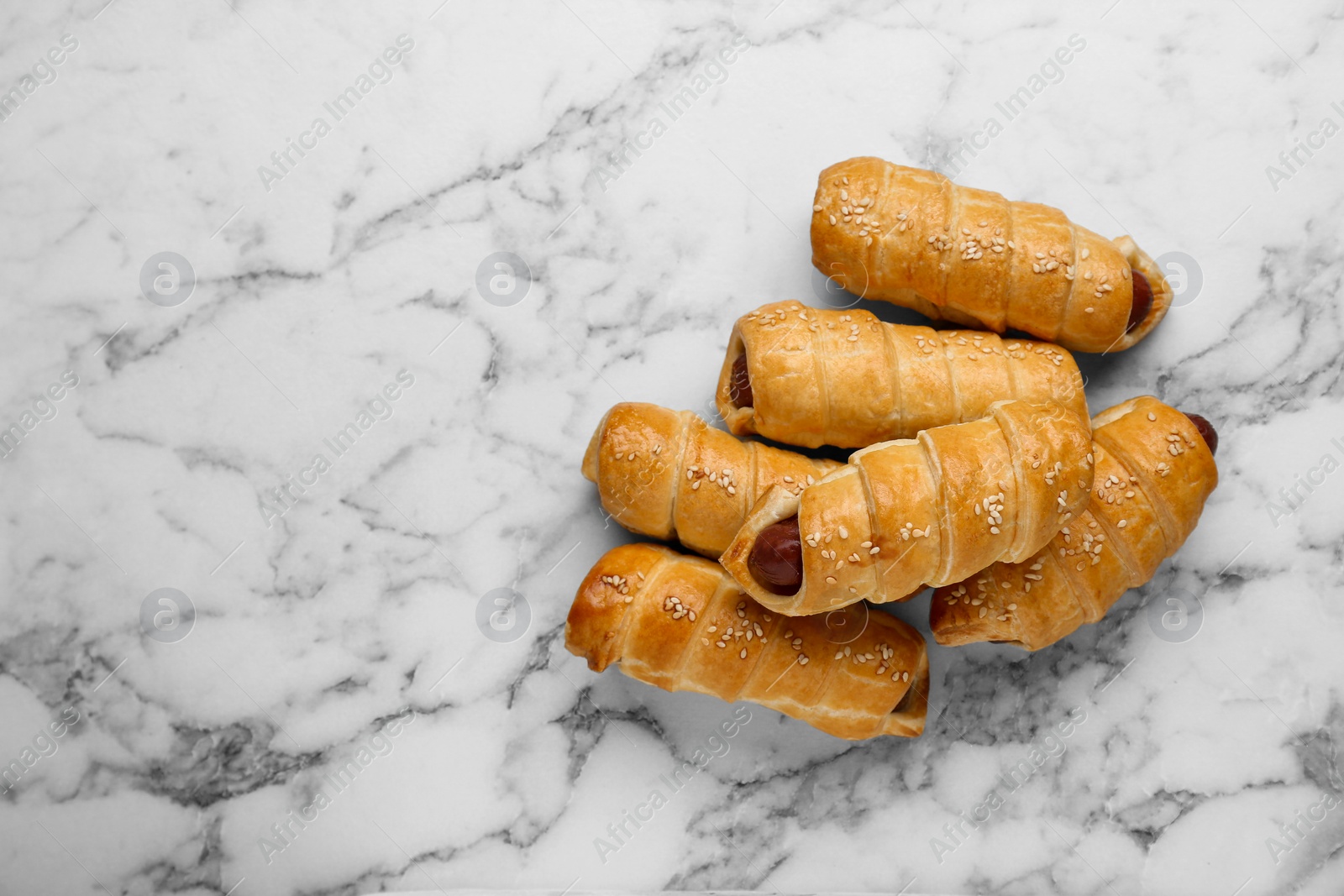 Photo of Delicious sausage rolls on white marble table, flat lay. Space for text