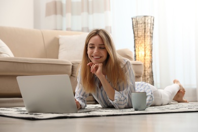 Pretty young woman with laptop lying on floor at home