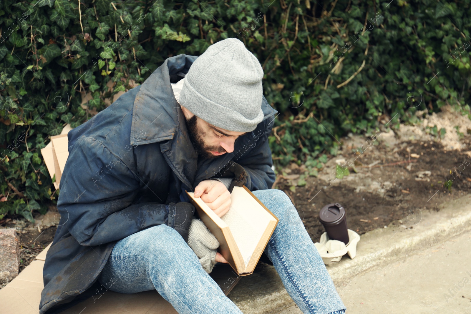 Photo of Poor homeless man with book on street in city