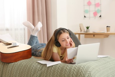 Photo of Teenage girl with headphones reading on bed at home