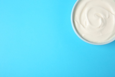 Bowl of sour cream on light blue background, top view. Space for text