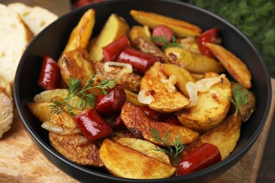 Photo of Delicious baked potato with thin dry smoked sausages, onion and dill in bowl on table, closeup