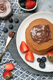 Photo of Tasty pancakes with chocolate paste and berries served on grey table, flat lay