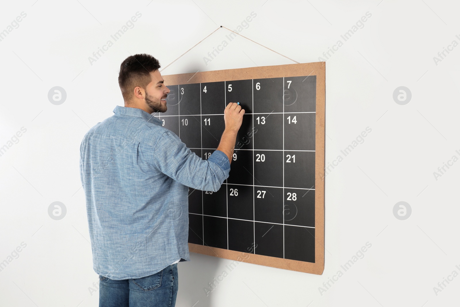Photo of Young man writing with chalk on board calendar