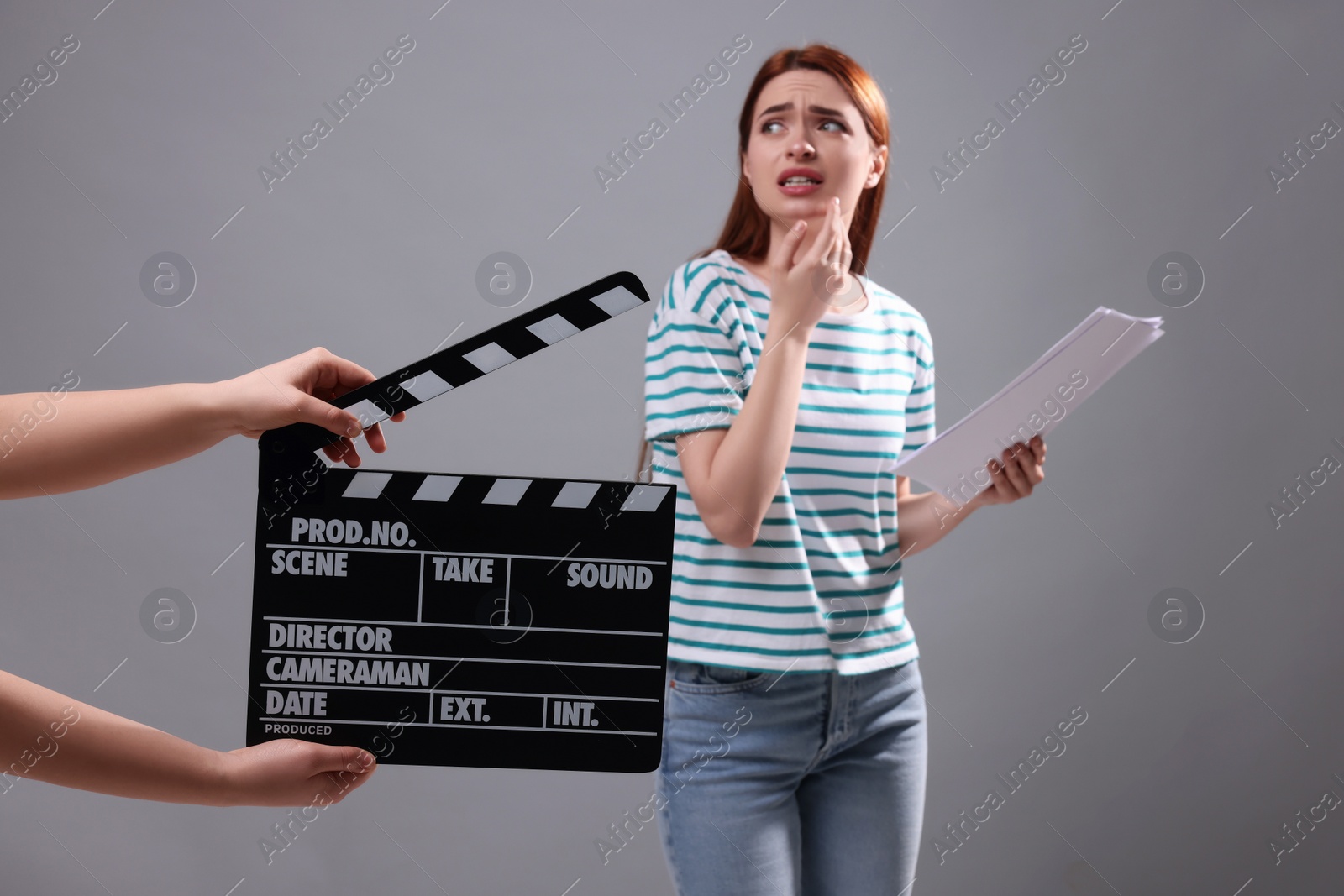 Photo of Emotional actress performing role while second assistant camera holding clapperboard on grey background, selective focus