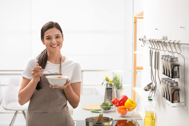 Photo of Young woman eating tasty vegetable soup in kitchen