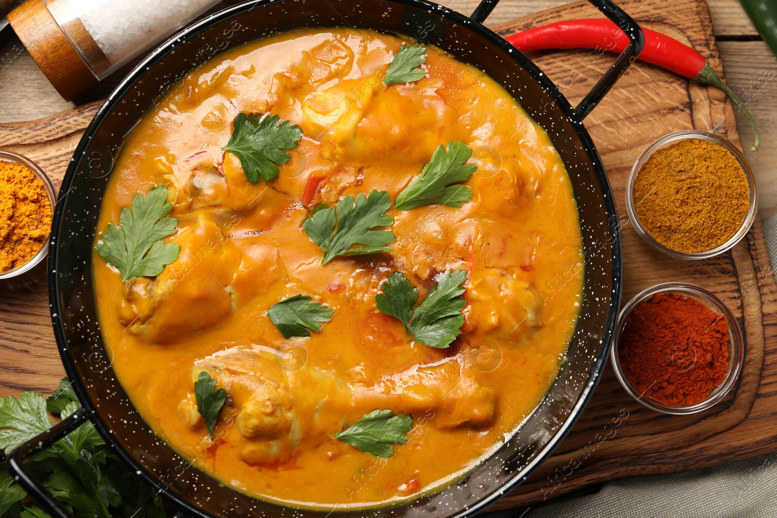 Photo of Tasty chicken curry with parsley and ingredients on wooden table, flat lay