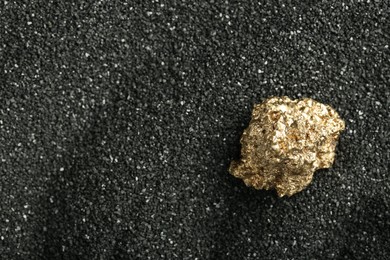 Shiny gold nugget on black sand, top view. Space for text