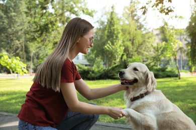 Photo of Cute golden retriever dog giving paw to young woman in park