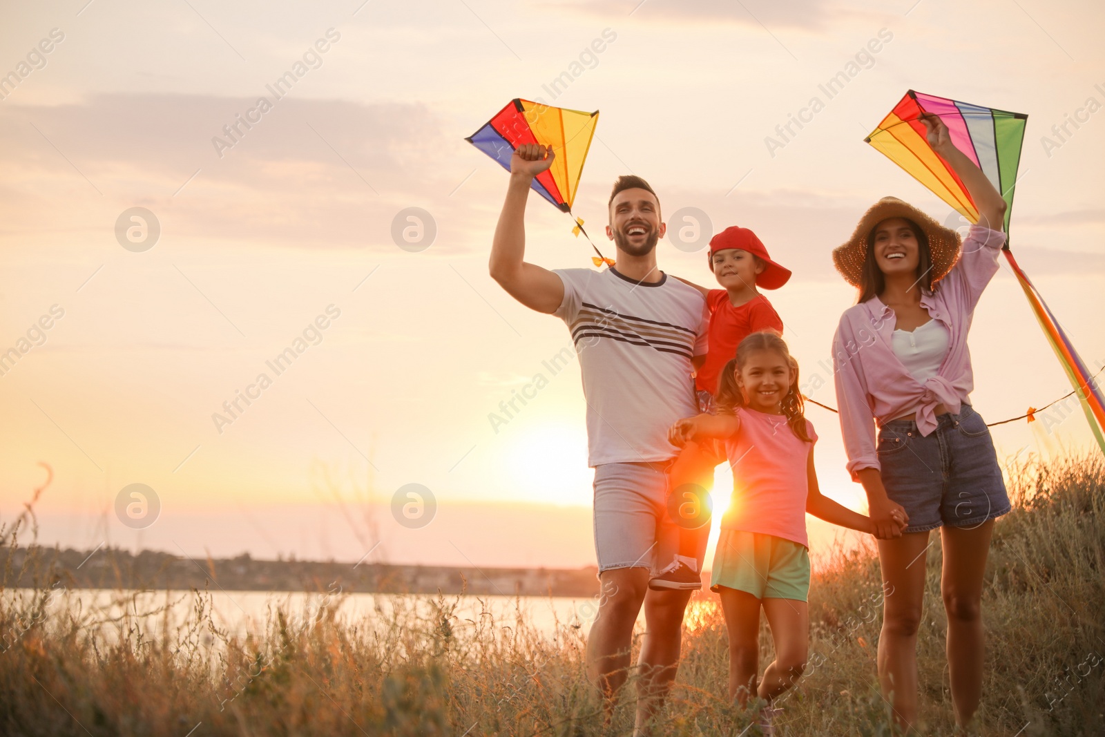 Photo of Happy parents and their children playing with kites outdoors at sunset. Spending time in nature