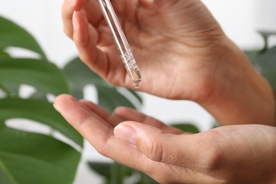 Photo of Woman applying cosmetic serum onto her hand near green plant on white background, closeup
