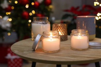 Burning candles on wooden table in room decorated for Christmas