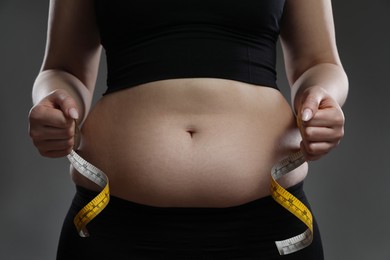 Photo of Woman measuring belly with tape on grey background, closeup. Overweight problem