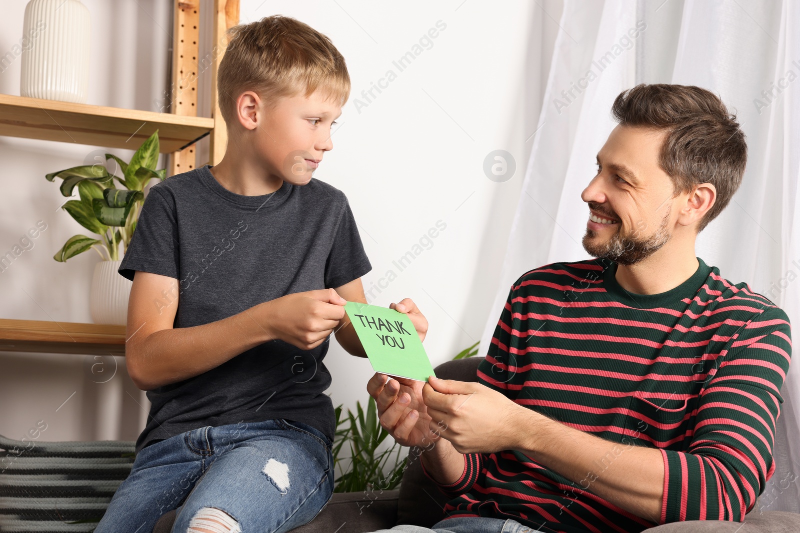 Photo of Happy man receiving greeting card from his son at home