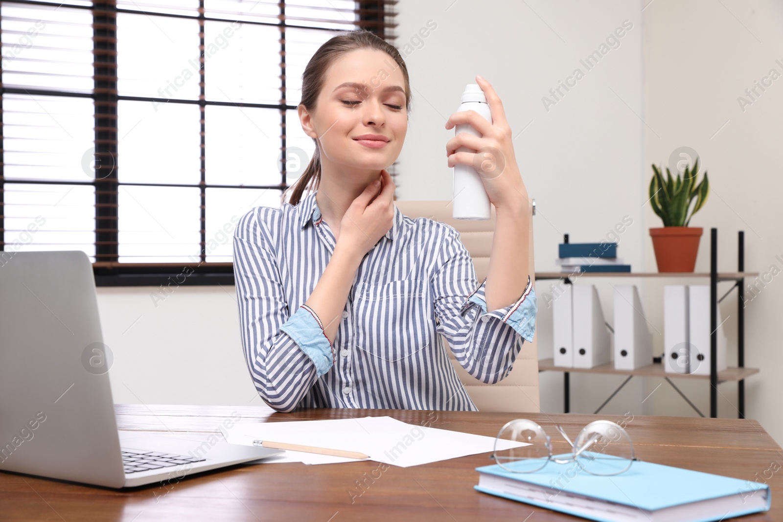 Photo of Young woman applying thermal water on face in office. Cosmetic product