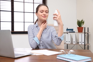 Young woman applying thermal water on face in office. Cosmetic product