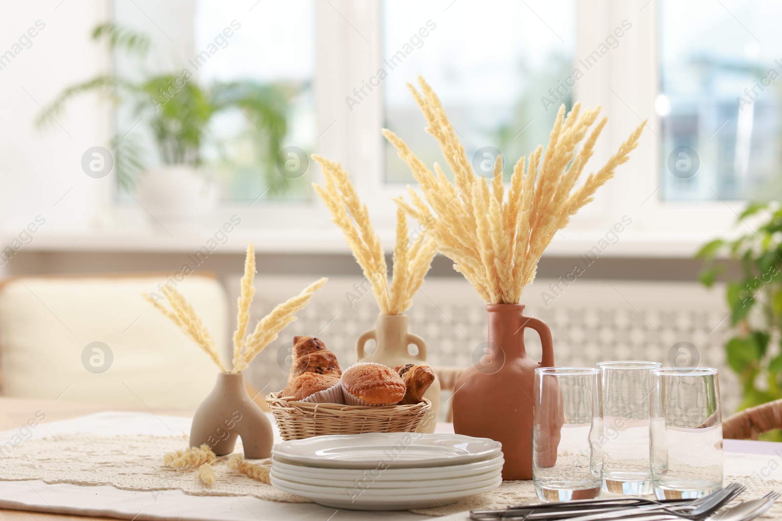 Photo of Clean dishes, dry spikes and fresh pastries on table in stylish dining room