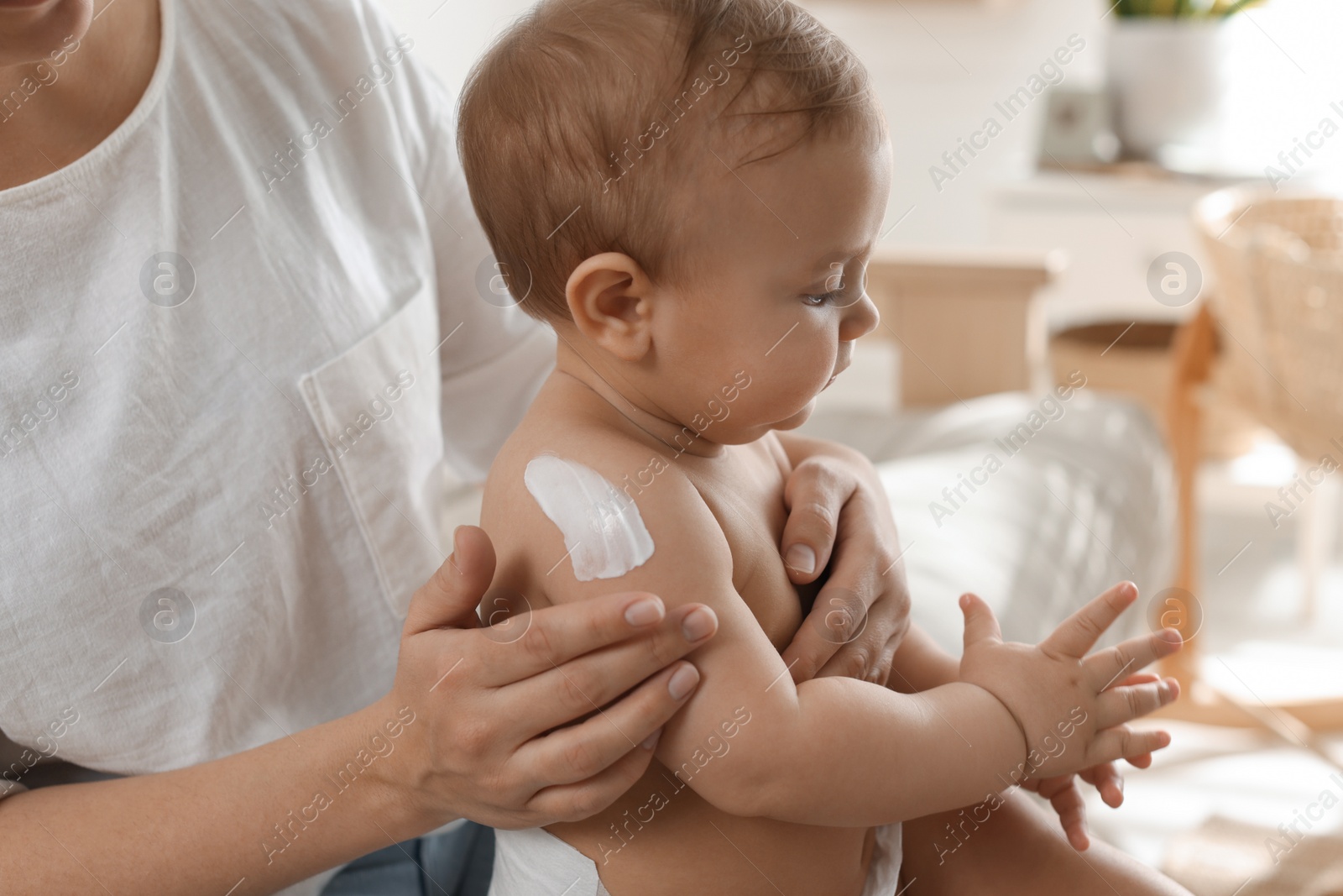 Photo of Mother applying body cream on her little baby at home, closeup