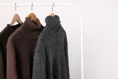 Photo of Rack with different casual sweaters on light background. Space for text
