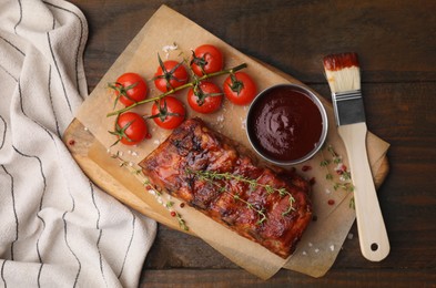 Photo of Tasty roasted pork ribs served with sauce and tomatoes on wooden table, top view