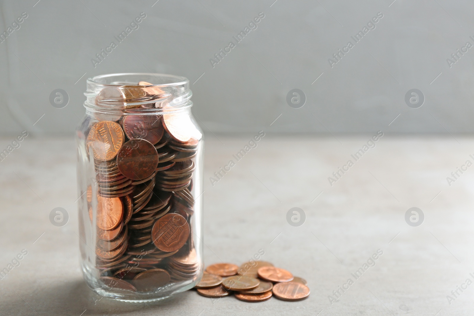 Photo of Glass jar and coins on table against grey background. Space for text