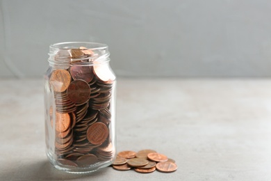 Photo of Glass jar and coins on table against grey background. Space for text