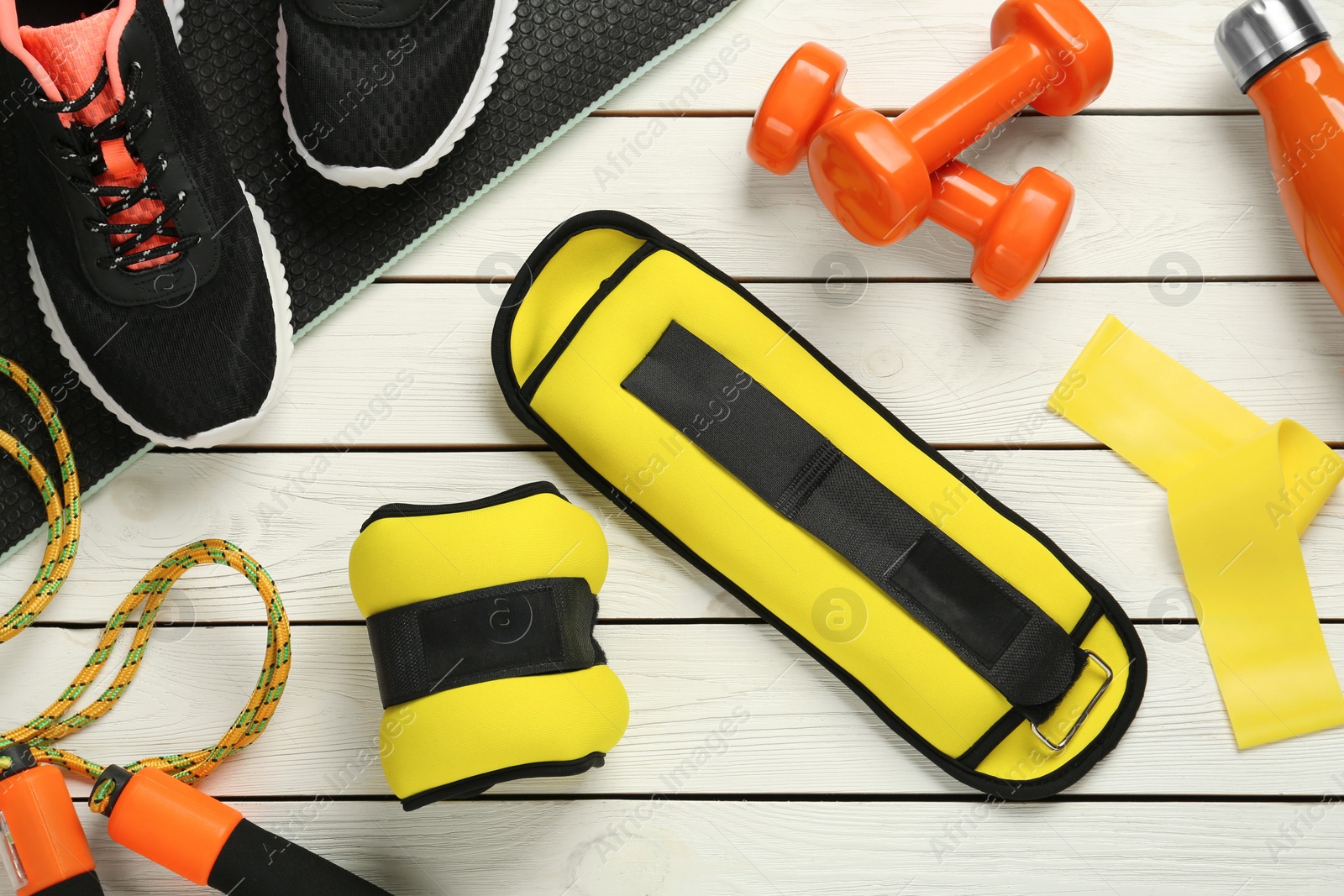 Photo of Yellow weighting agents and sport equipment on white wooden table, flat lay