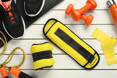 Photo of Yellow weighting agents and sport equipment on white wooden table, flat lay