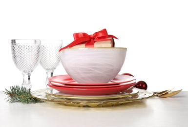 Festive dishware with gift, glasses and Christmas decorations on white table