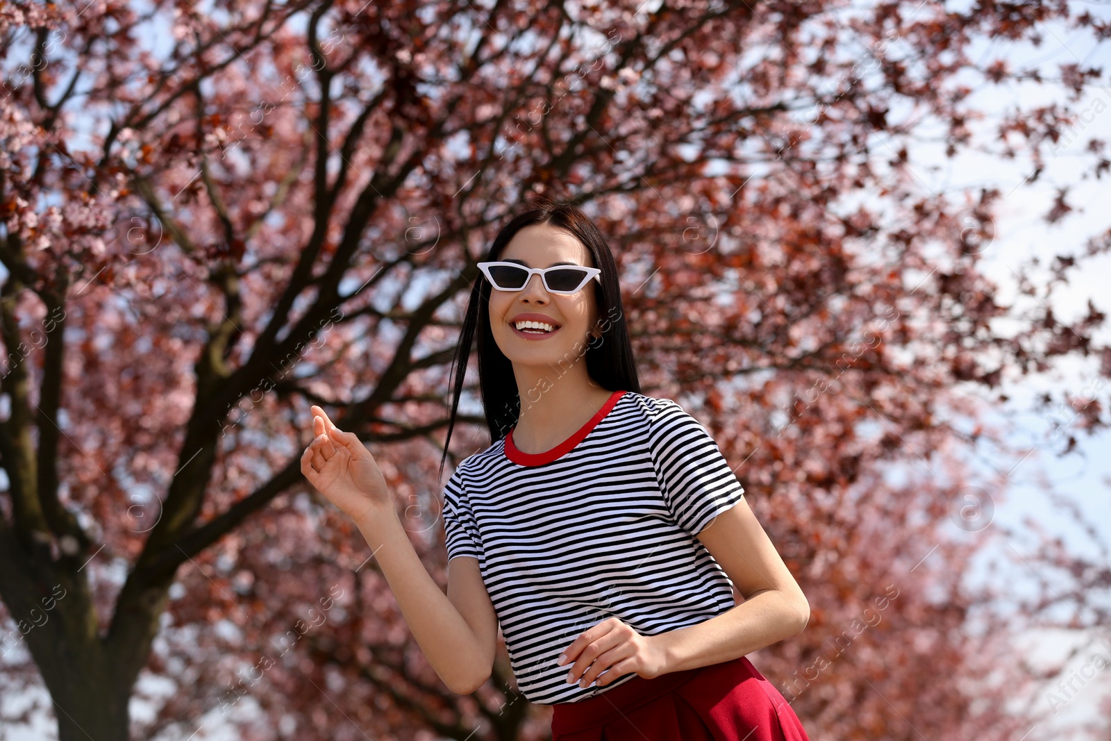 Photo of Pretty young woman with sunglasses near beautiful blossoming trees outdoors. Stylish spring look