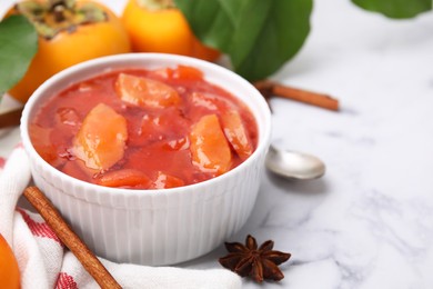 Photo of Bowl of tasty persimmon jam and ingredients on white marble table. Space for text