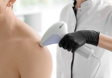 Man undergoing hair removal procedure with photo epilator in salon