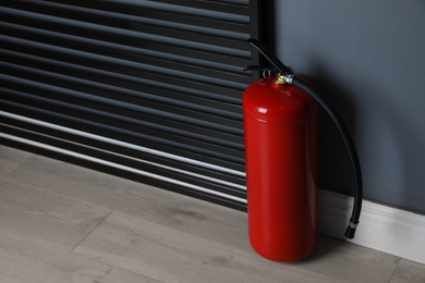 Fire extinguisher near grey wall indoors. Space for text