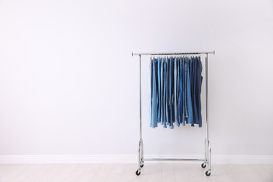 Photo of Rack with different jeans near light wall. Space for text