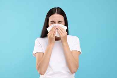 Photo of Suffering from allergy. Young woman blowing her nose in tissue on light blue background