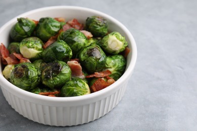 Photo of Delicious roasted Brussels sprouts and bacon in bowl on grey table, closeup. Space for text