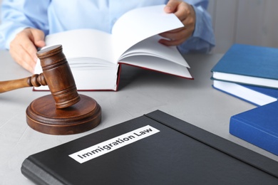 Photo of Folder with words IMMIGRATION LAW, gavel and blurred person on background