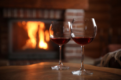 Photo of Glasses of wine blurred fireplace on background, space for text. Winter vacation