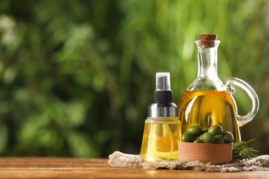 Photo of Bottles with cooking oil, olives and rosemary on wooden table against blurred background. space for text
