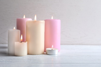 Different wax candles burning on table against light background