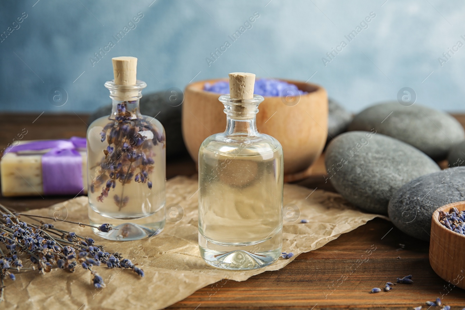 Photo of Bottles with natural herbal oil and lavender flowers on table against blurred background