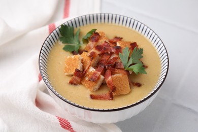 Delicious lentil soup with bacon and parsley in bowl on white tiled table, closeup